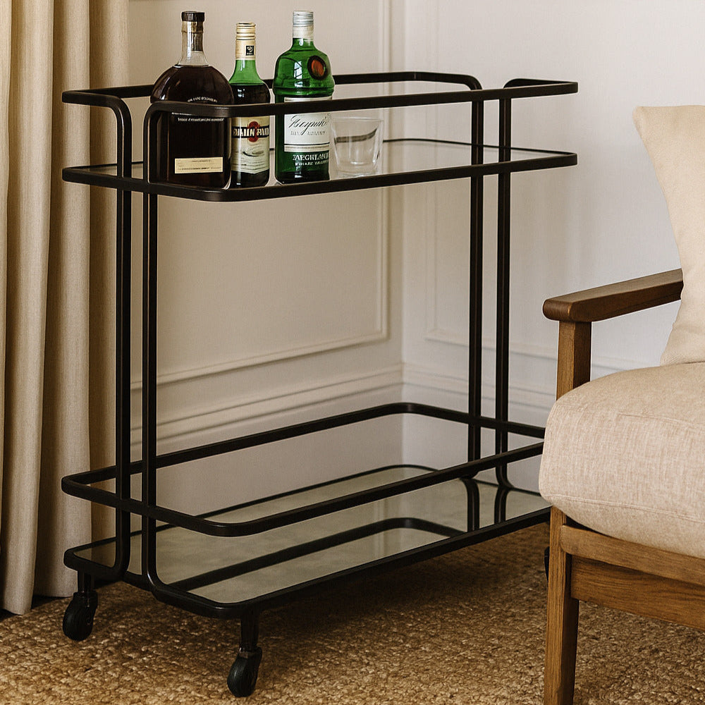 Bar cart with bottles in a room with a chair and beige curtains.