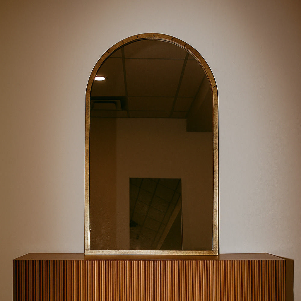 Wooden console table with an arched mirror on a plain wall.