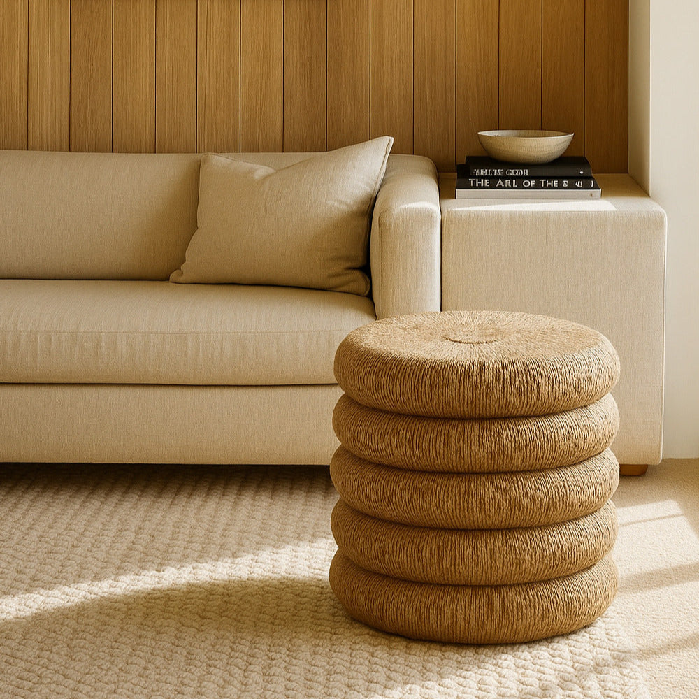 Beige sofa with a woven stool in a room with wooden paneling and a beach painting.