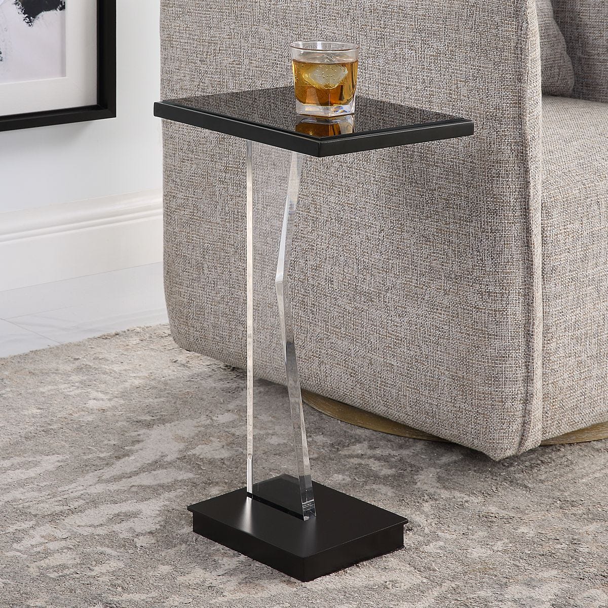 Black side table with a glass of whiskey against a gray sofa.