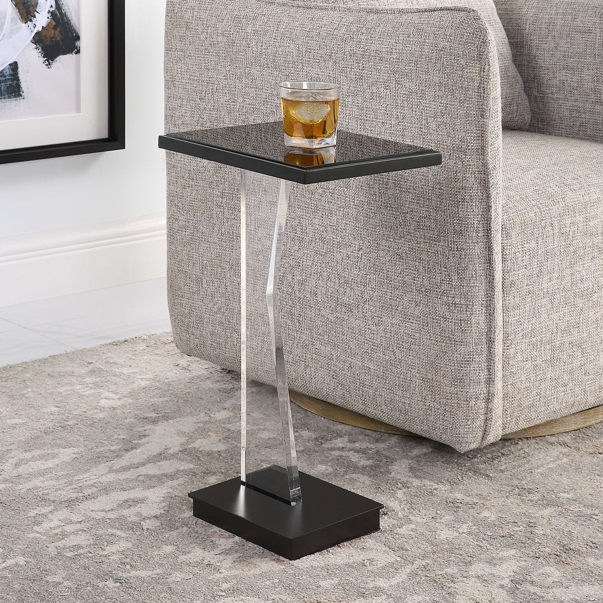Black side table with a glass of whiskey next to a gray sofa.