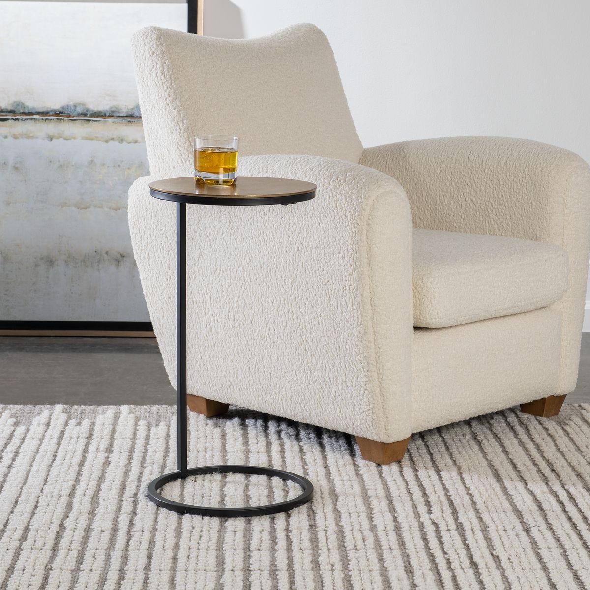 Beige armchair with a small round table and a glass of water on a neutral background