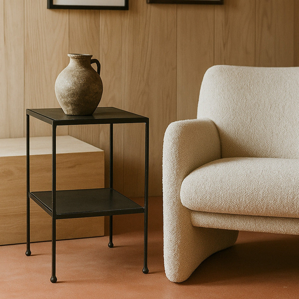Beige armchair next to a black side table with a vase and two framed pictures on a wooden wall.