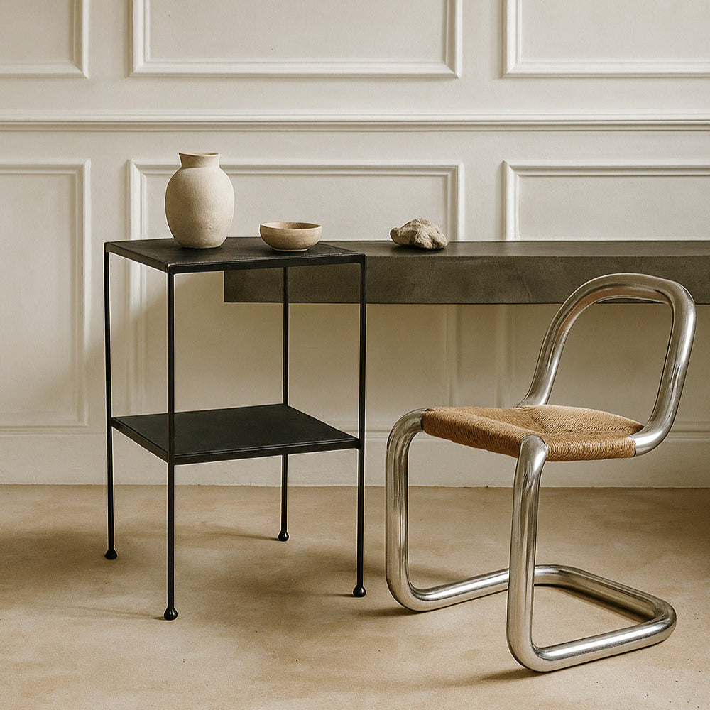 Modern chair with a metal frame and wooden seat next to a small table against a neutral wall.