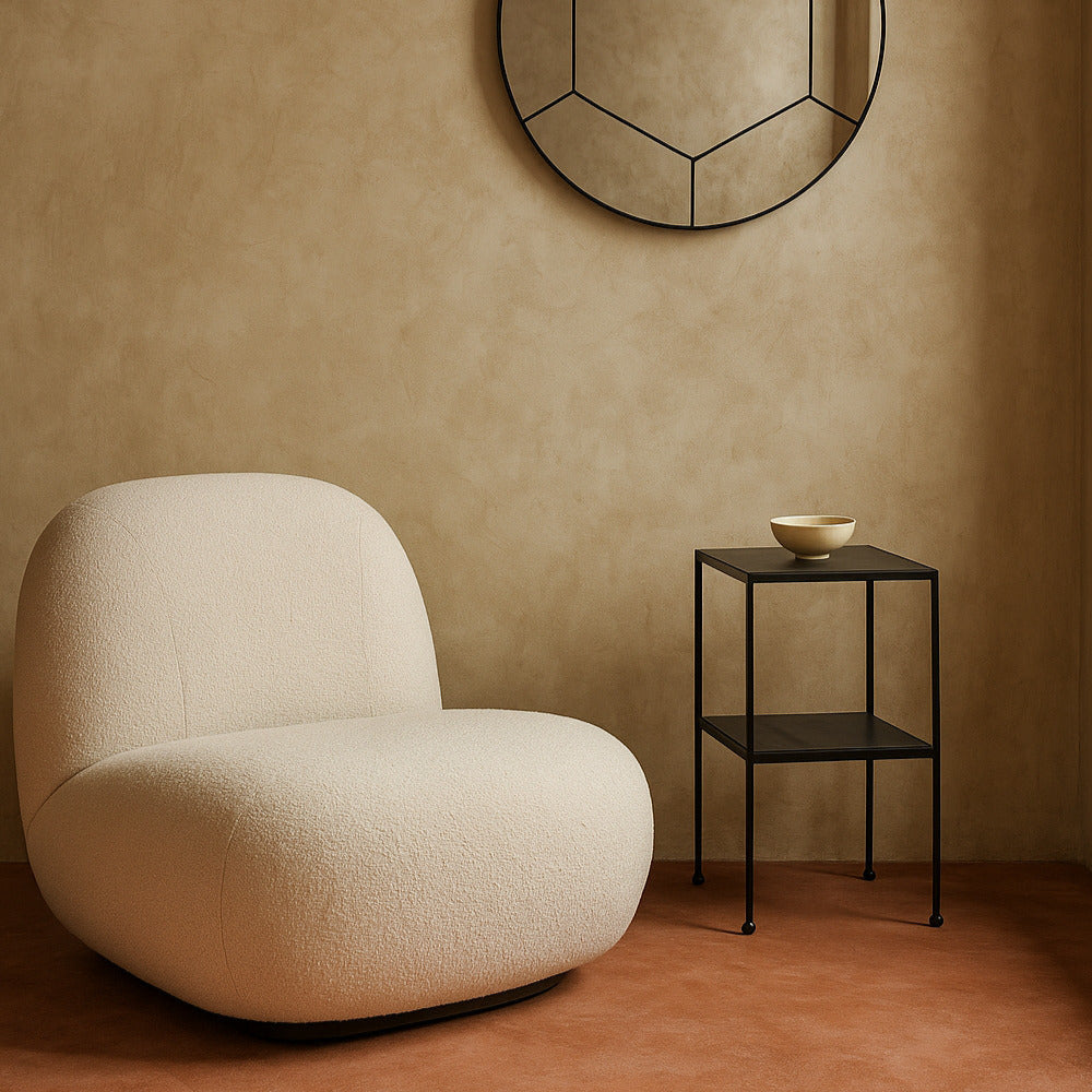 Beige armchair and small black side table against a beige wall with a decorative mirror.
