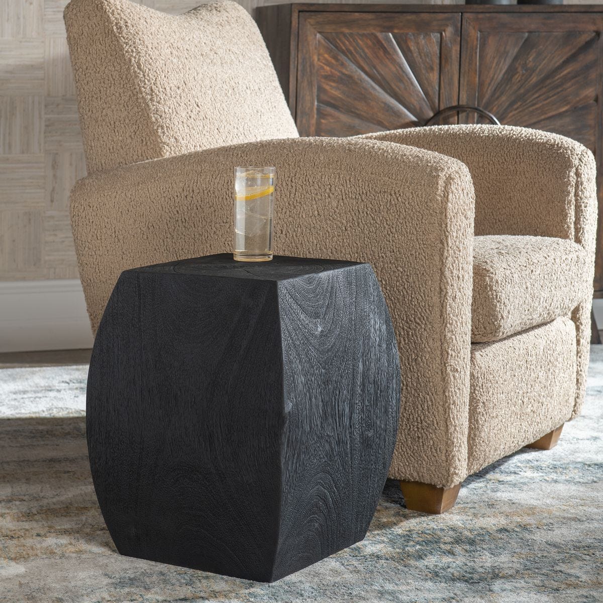 Black side table with a glass of water next to a beige armchair in a room.
