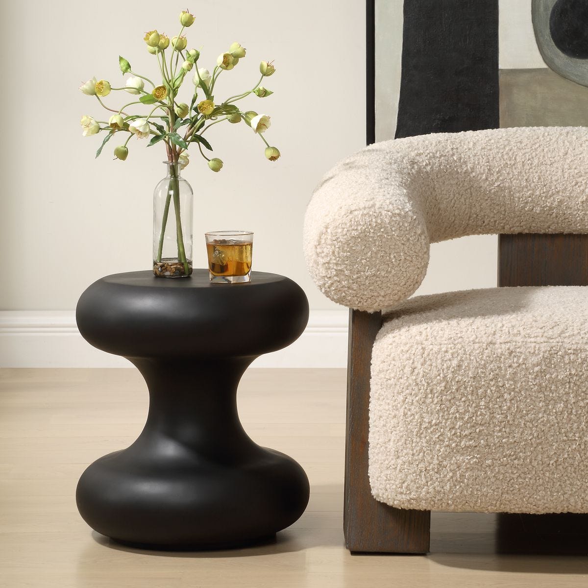 Black side table with a glass of tea and vase of flowers next to a textured chair.