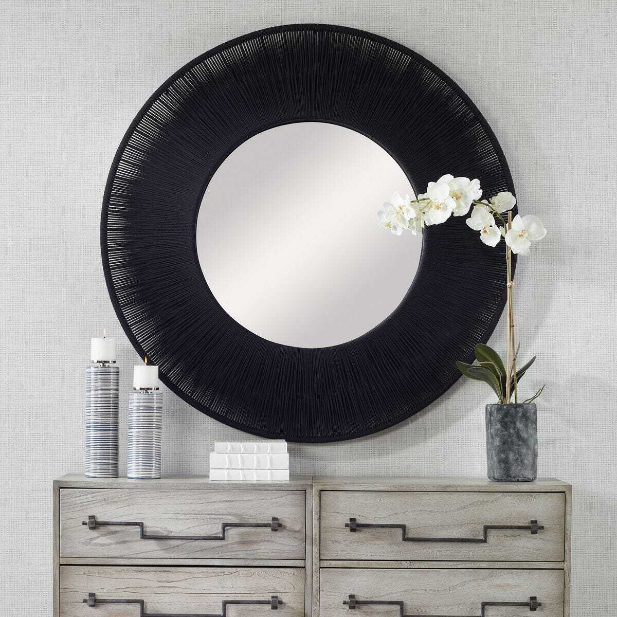 Round black-framed mirror on a wall above a wooden dresser with decorative items.