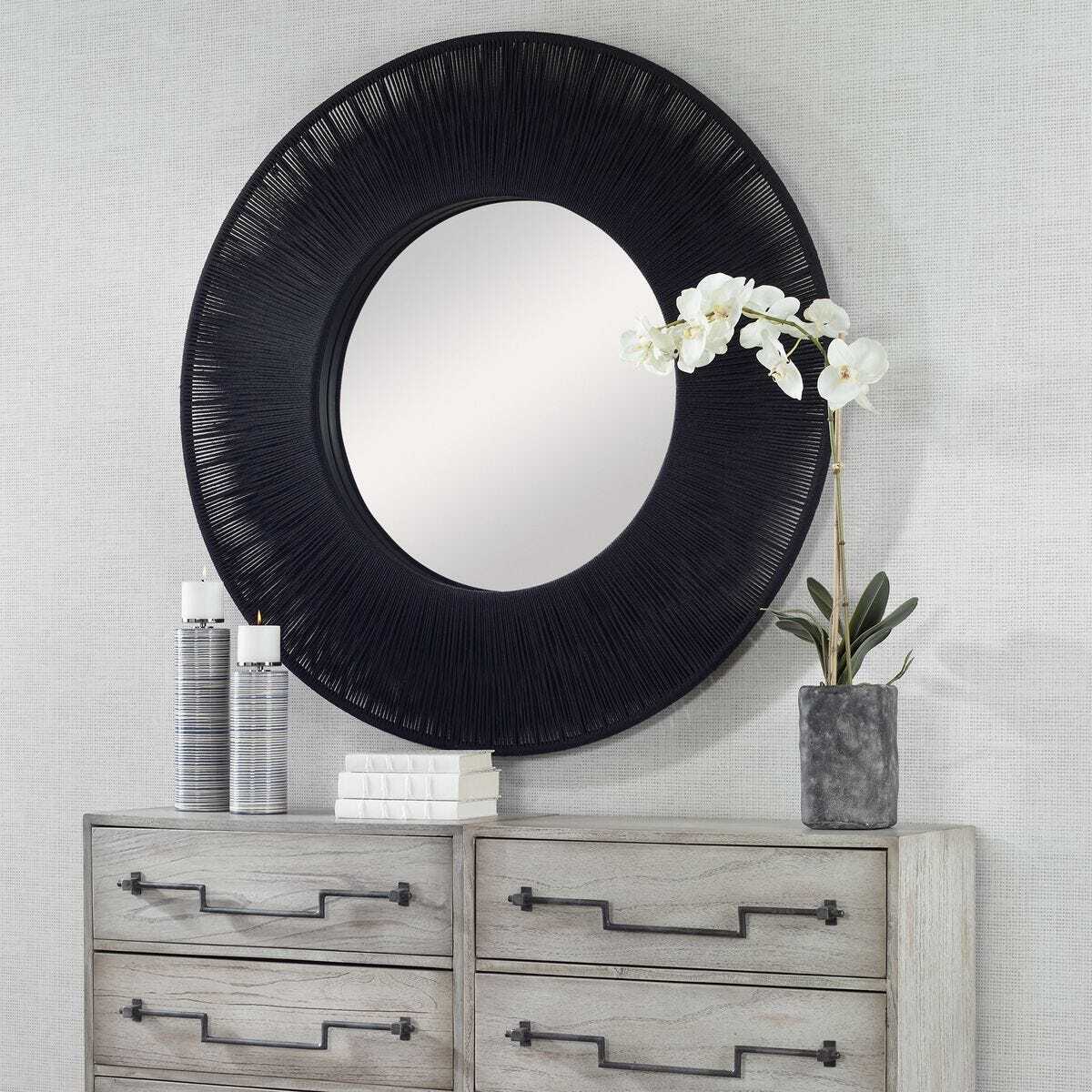 Round black-framed mirror on a gray wall above a wooden dresser with decorative items.