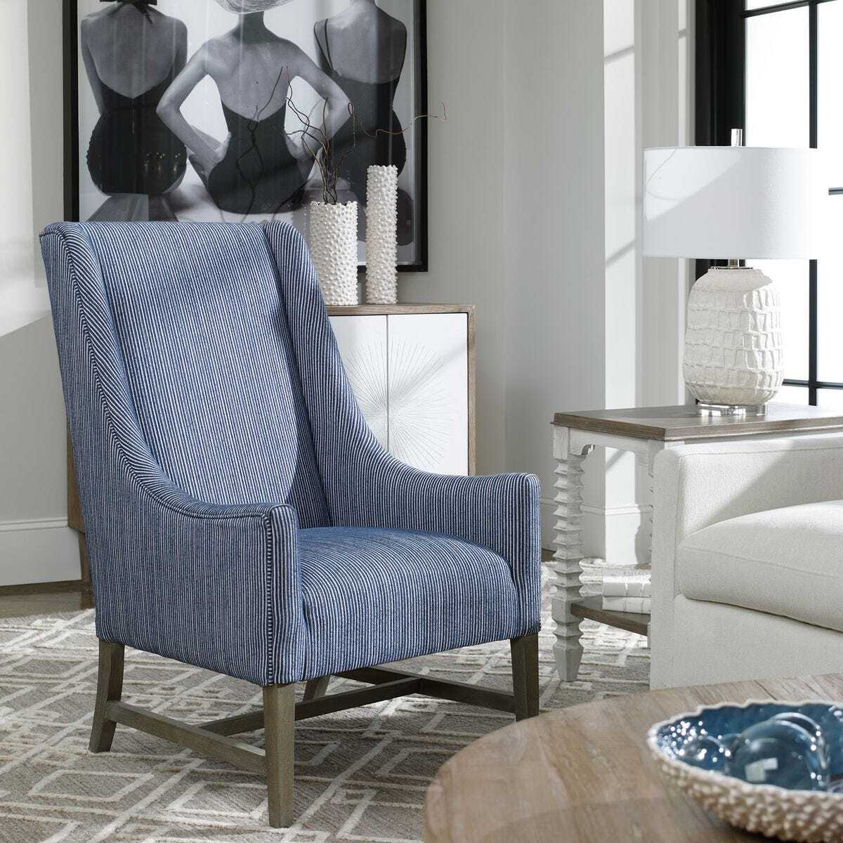 Blue armchair in a living room setting with a lamp and artwork on the wall.