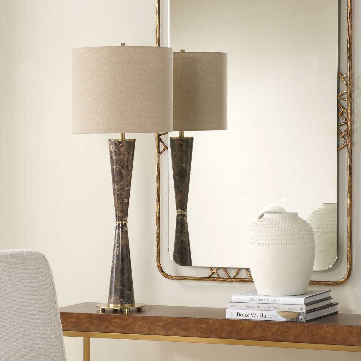 Decorative table lamp with a mirror and books on a console table.