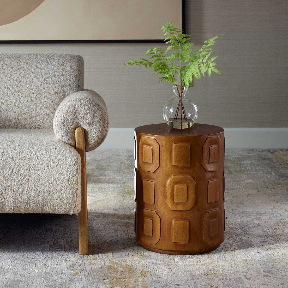 Brown textured side table with a plant next to a textured armchair in a room.