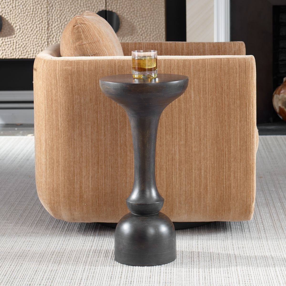 Small black side table with a glass of water in front of a beige armchair.
