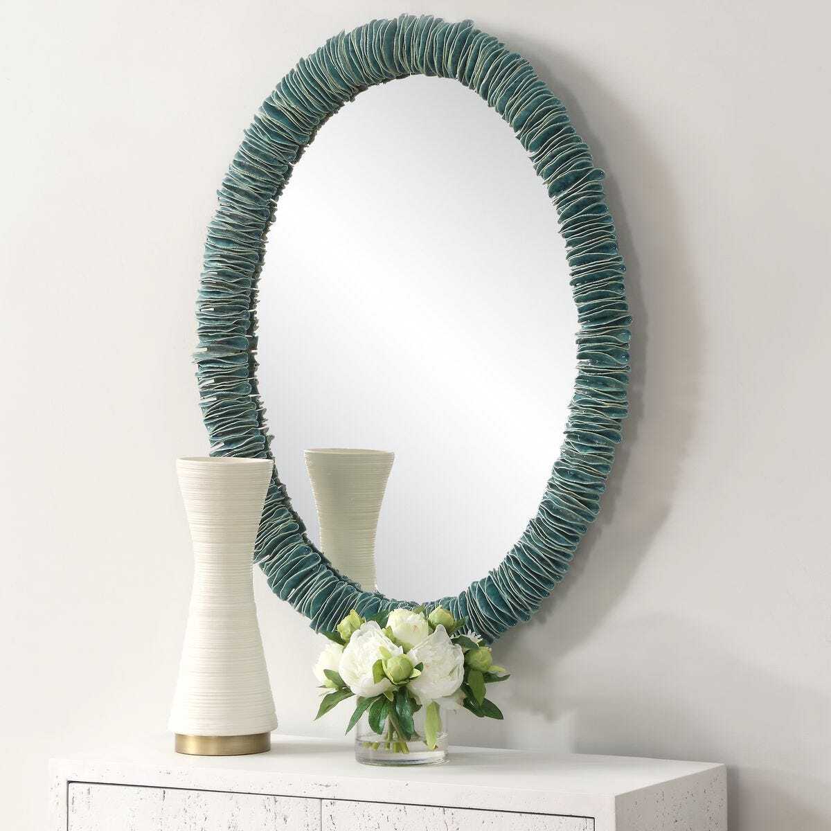 Round mirror with teal woven frame on a white surface with decorative items.