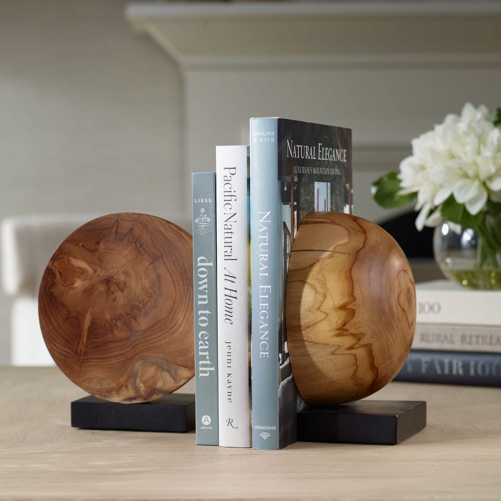 A pair of mid century modern bookends made of teak wood with black bases, holding up a couple of books on a shelf.