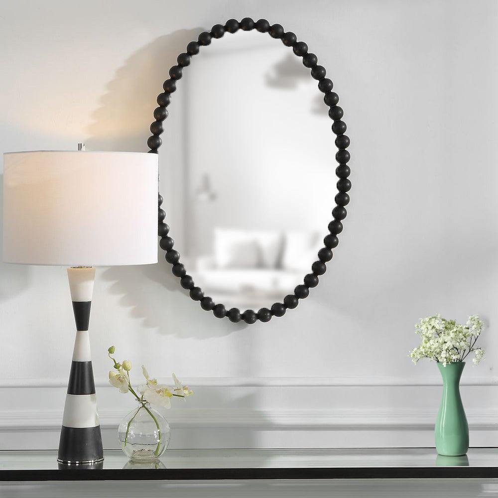 Entryway mirror with black frame with decorative circle and a glass console table with lamp and vase.