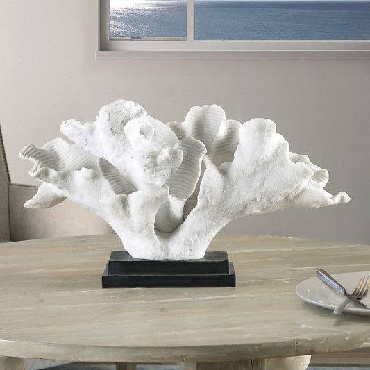 White coral statue in entryway on rattan coastal console table with ocean art hung above and a white rug.