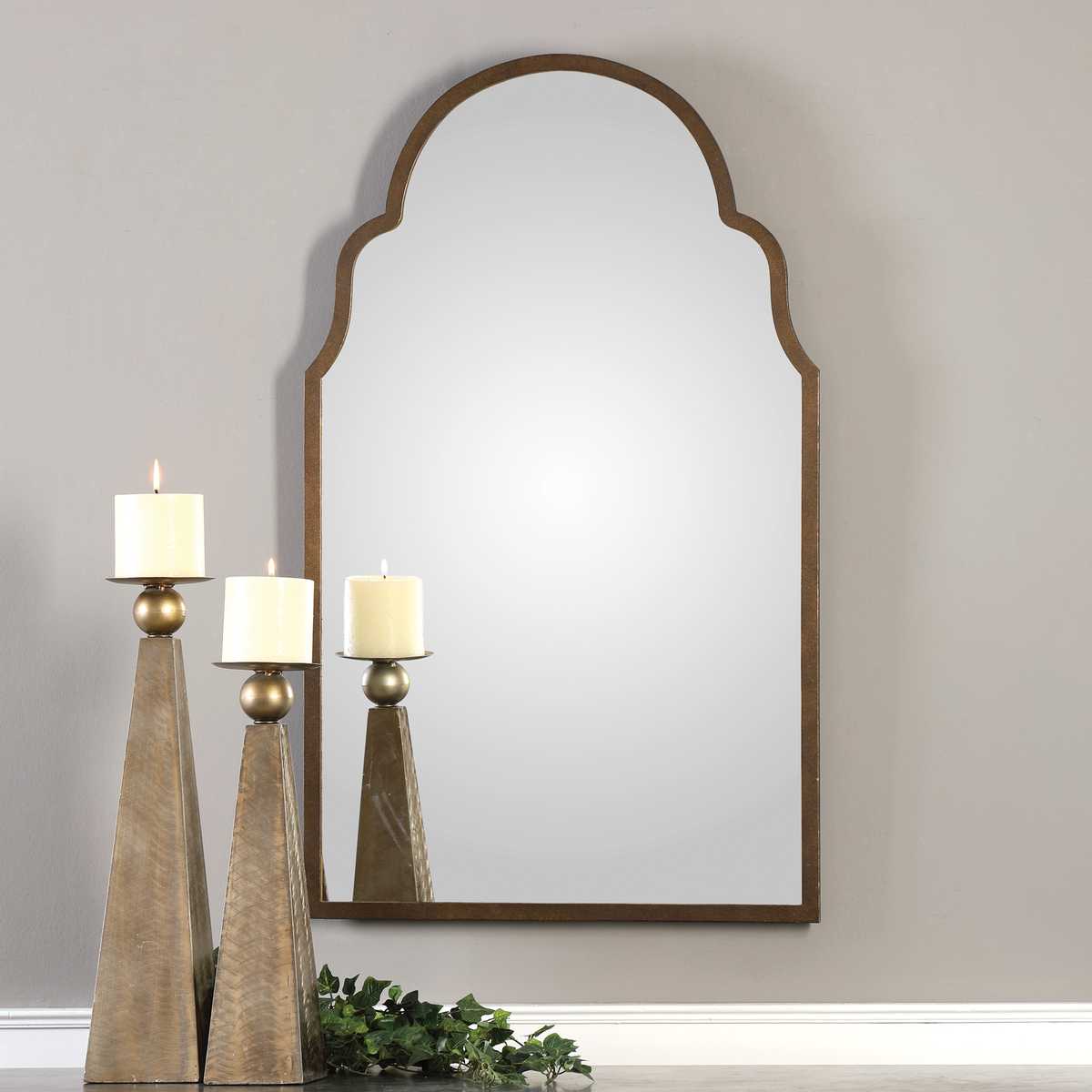 Decorative mirror with arched top on a wall above candles and greenery
