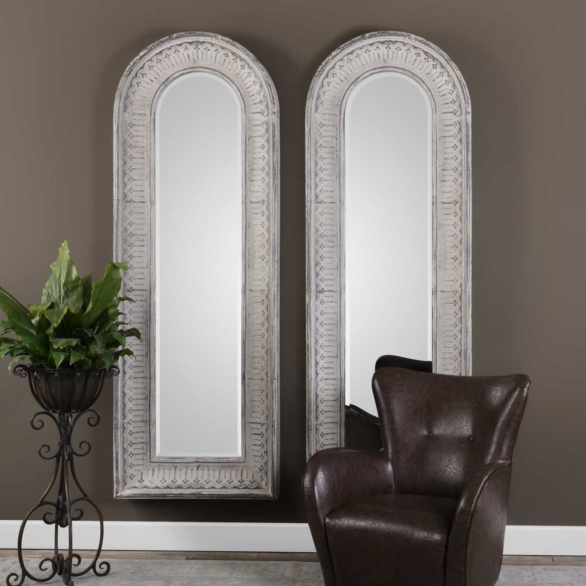 Two ornate wall mirrors on a dark wall with a plant and chair in the foreground.