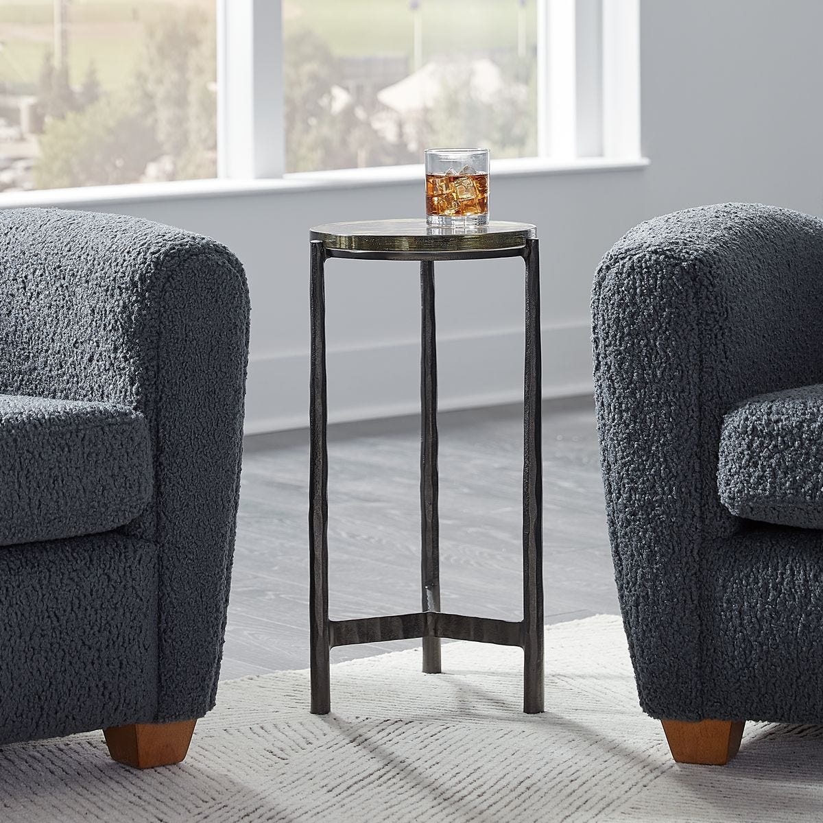Two gray armchairs with a small round table in a room with large windows.