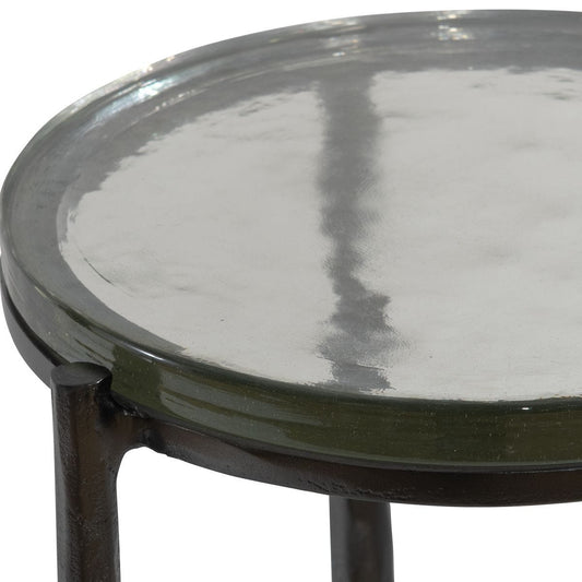 Small black side table with a glass of amber liquid next to a beige sofa against a patterned wall.