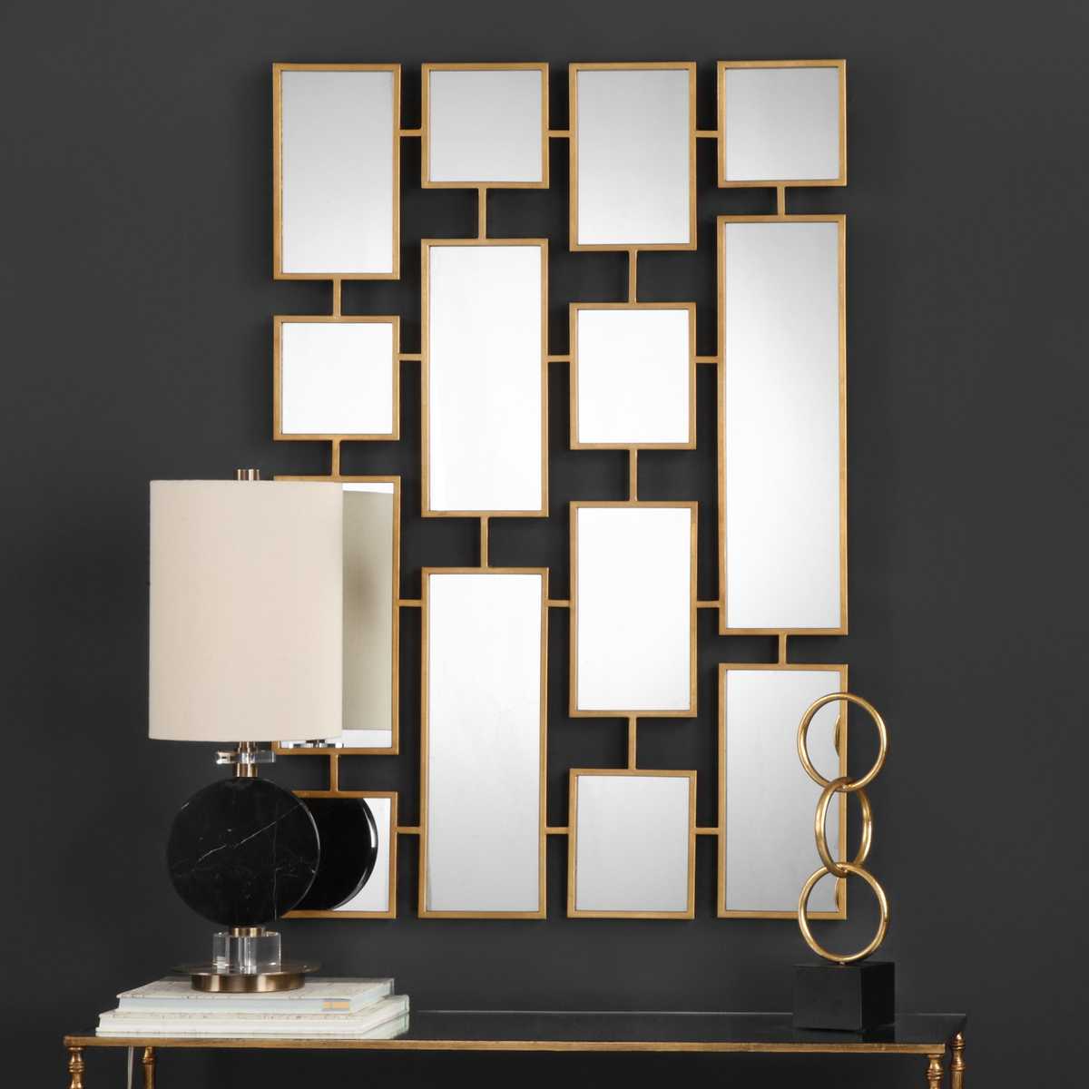 Decorative wall mirror with geometric design on a dark wall, accompanied by a lamp and books.