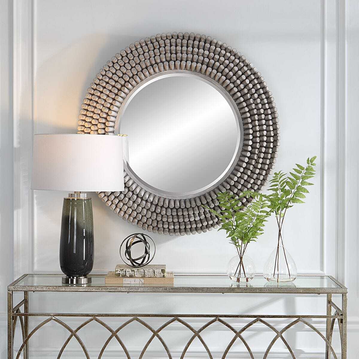 Decorative round mirror with a lamp and vases on a console table against a white wall.