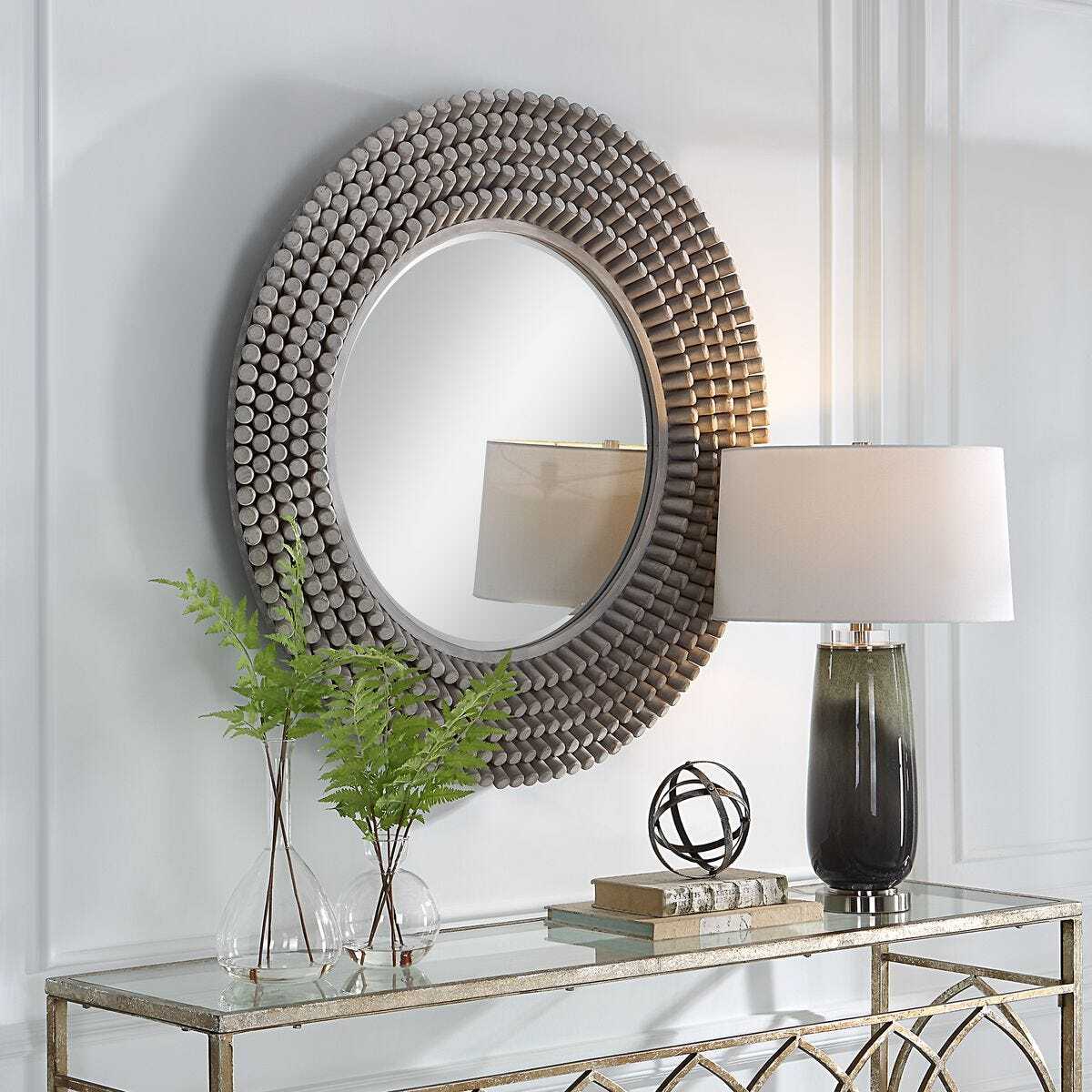 Decorative round mirror with a textured frame on a wall above a console table with a lamp and books.