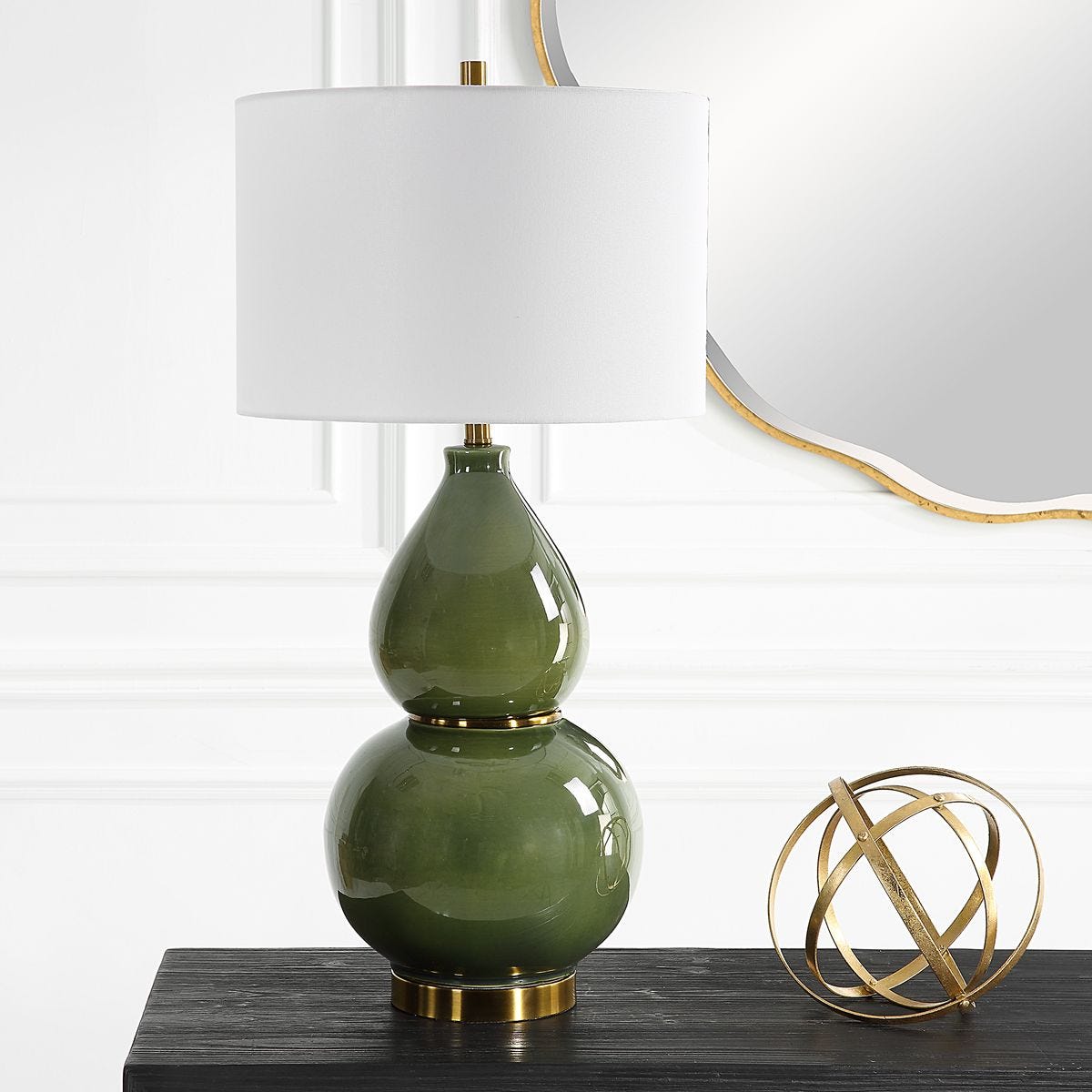 Green glass lamp with white shade on a table next to a gold decorative sphere.