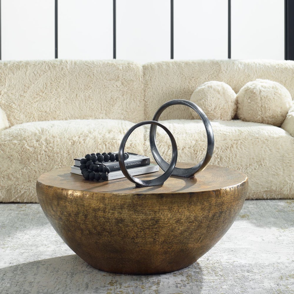 Hammered gold coffee table with accessories in a plush living room.