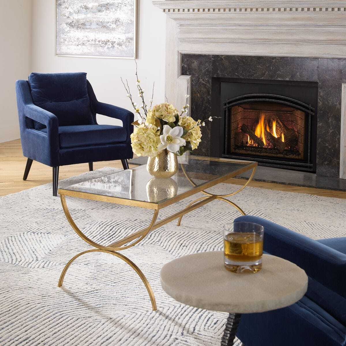 Living room with a fireplace, blue armchair, glass coffee table, and decorative items.