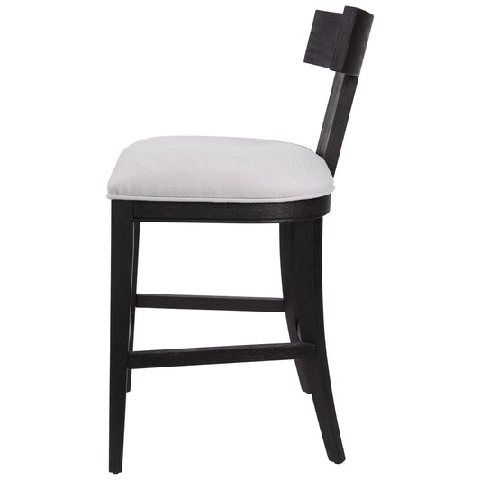 Klismos style counter stool featuring a curved charcoal black frame and a stone white cushion . Shows a grouping of stools seated along a long brown kitchen island.