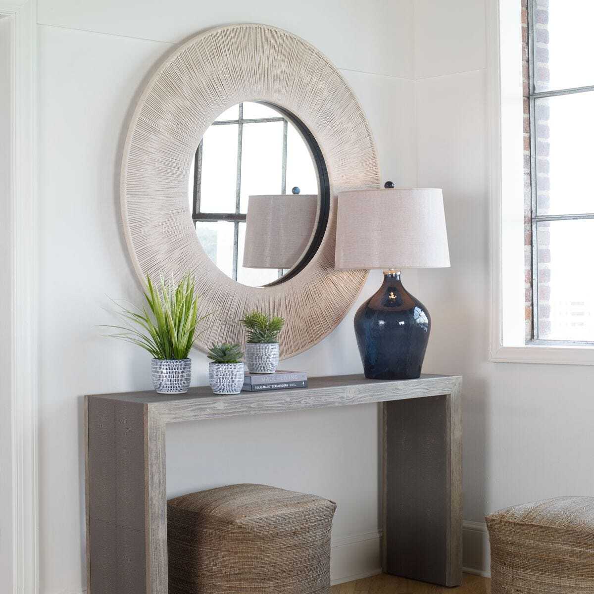 Decorative console table with round mirror, lamp, and plants in a room.
