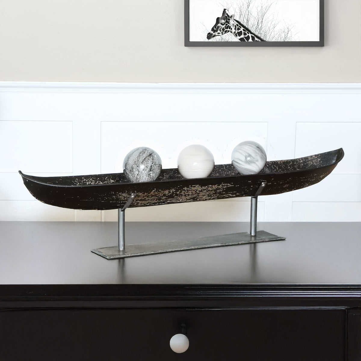 Modern distressed black decorative bowl with marble orbs inside and a piece of art with a Giraffe in it.