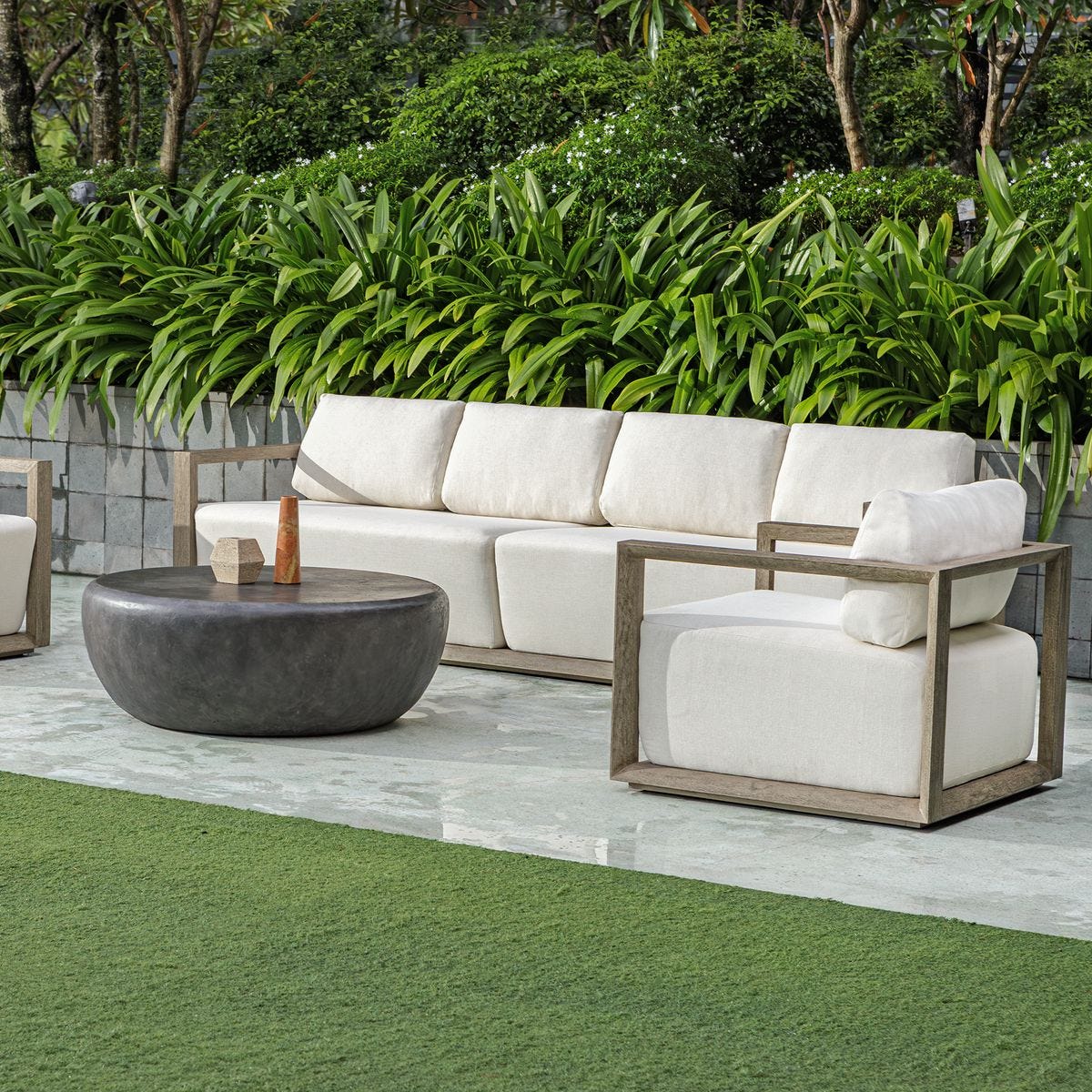 Outdoor patio set with white cushions and wooden frames on a patio with greenery in the background.