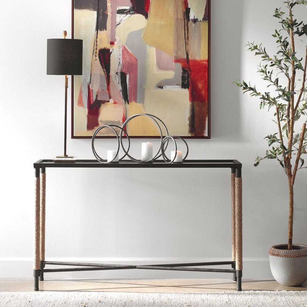 Console table with decorative items in a room with abstract art and a plant.