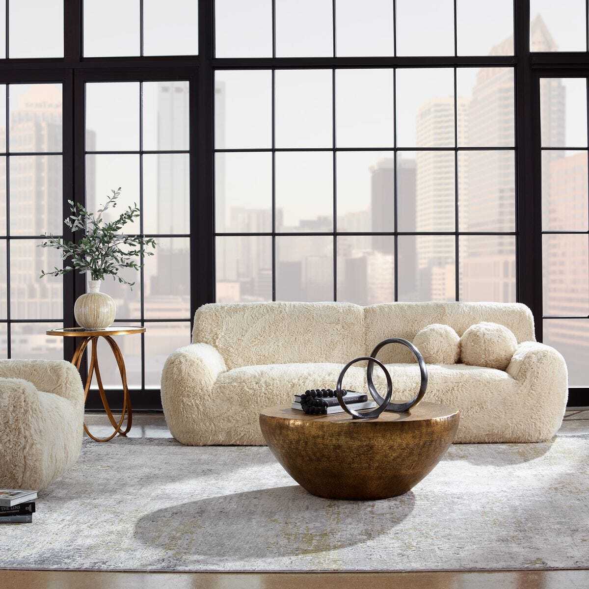 Modern living room with a beige sofa, round wooden coffee table, and large windows.