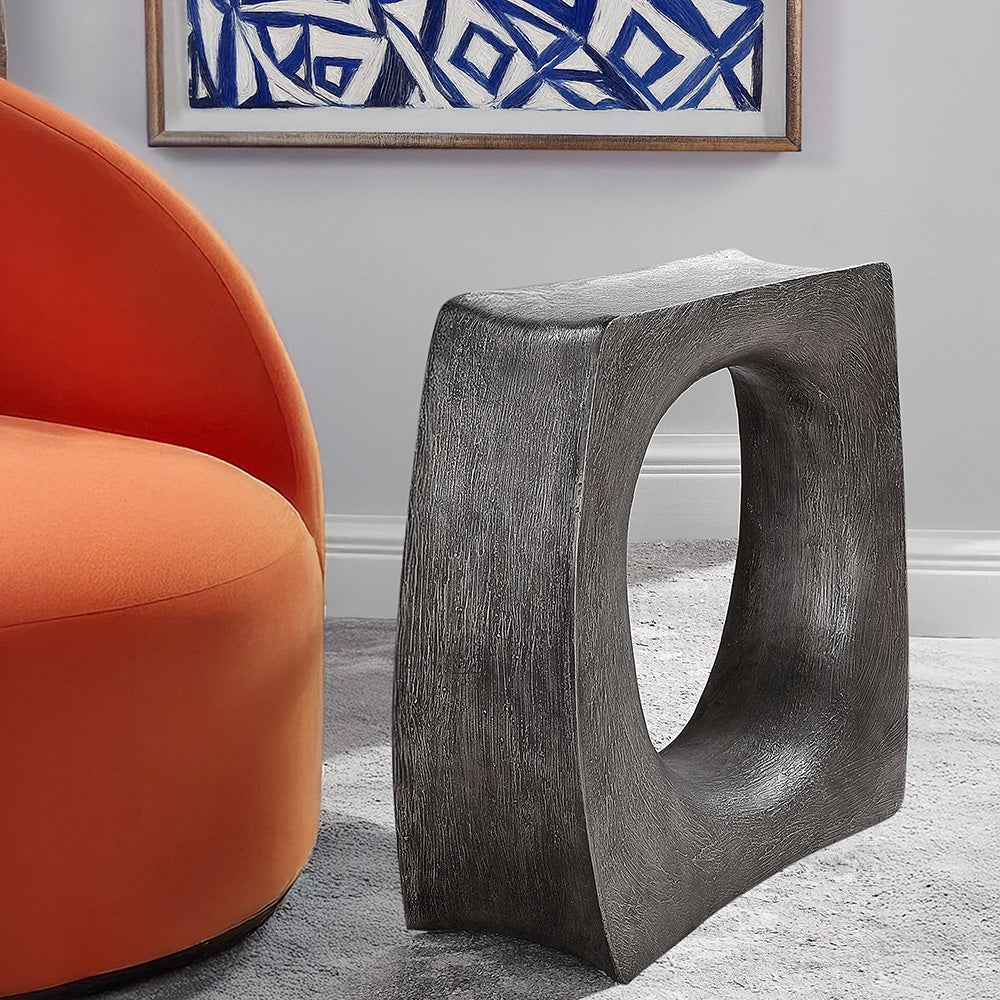Modern silver accent table to an orange chair in a living room with blue abstract art.