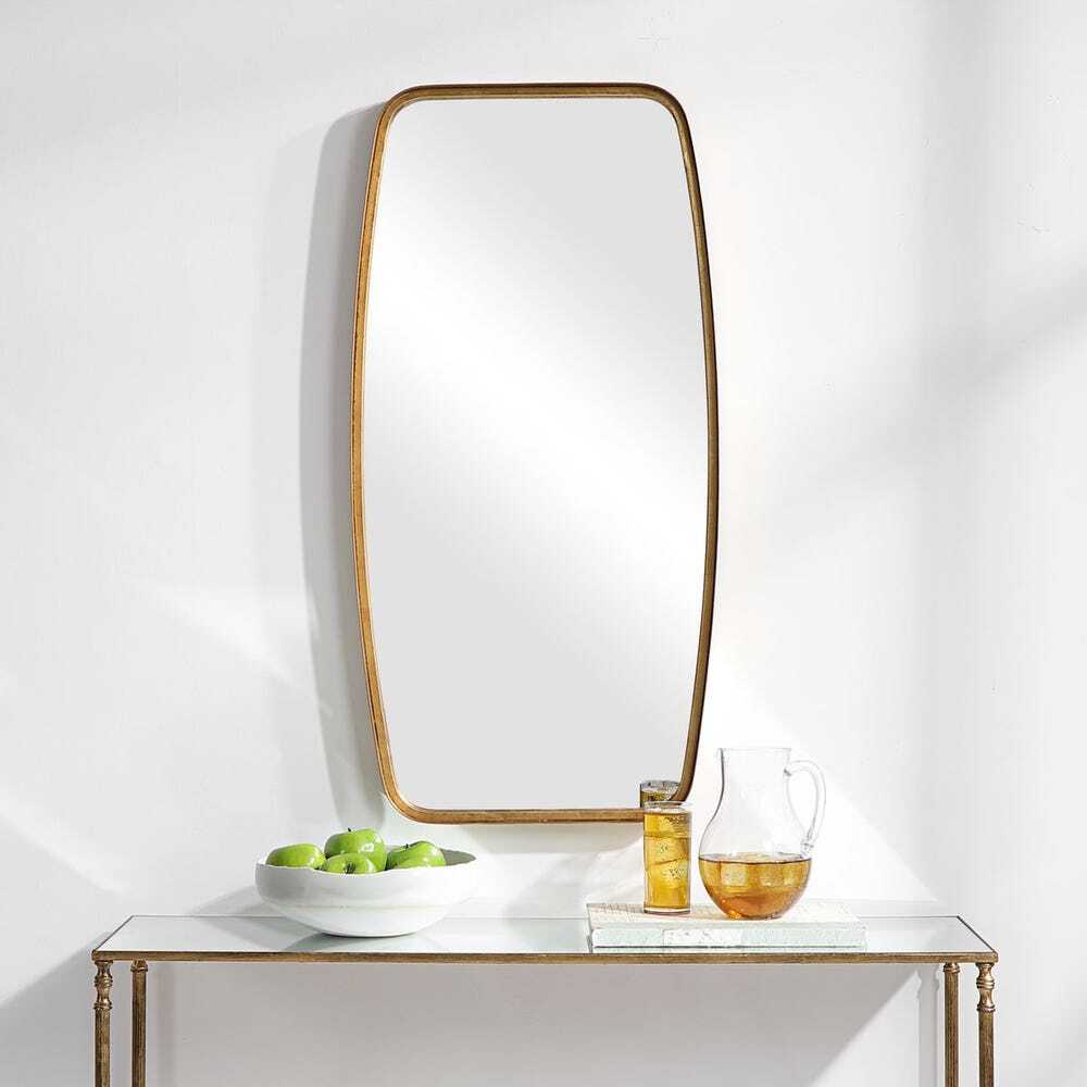 Gold-framed mirror on a white wall with a small table below holding a bowl of apples and a pitcher.