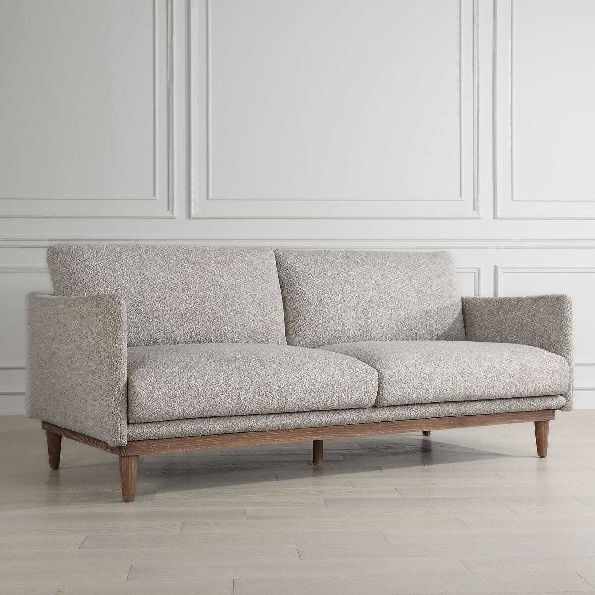 Gray sofa with wooden legs in a room with white paneled walls.