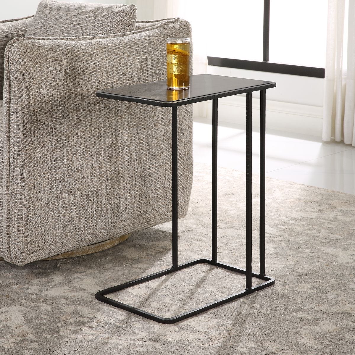 Small black side table next to a gray armchair with a glass of beer on a light-colored floor.