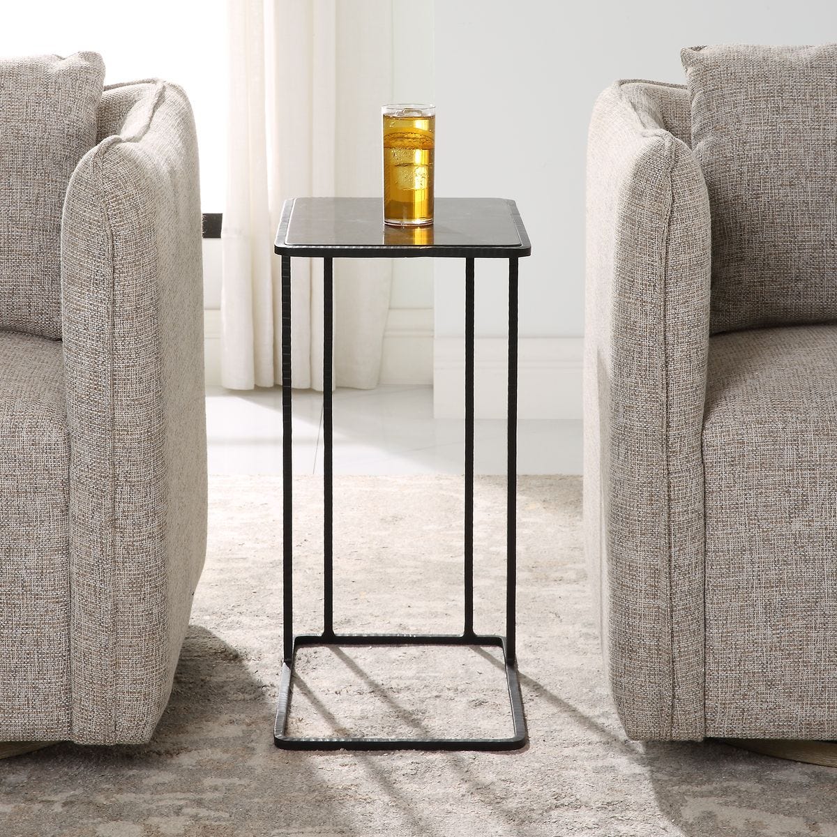 Small black side table with a glass of water between two gray armchairs in a living room.