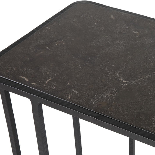 Small black side table next to a gray armchair with a glass of beer on a light-colored floor.