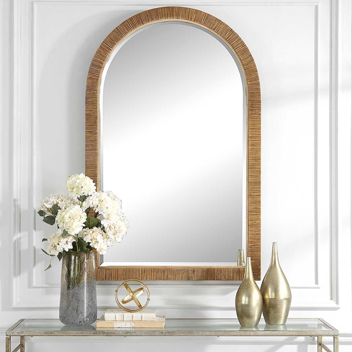 Decorative mirror with rattan frame above a console table with decorative items.