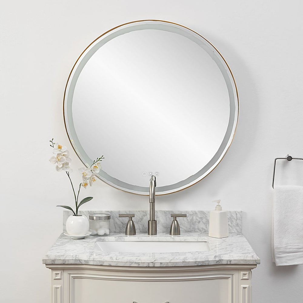 Lighted round gold mirror over a marble vanity with straight on view.