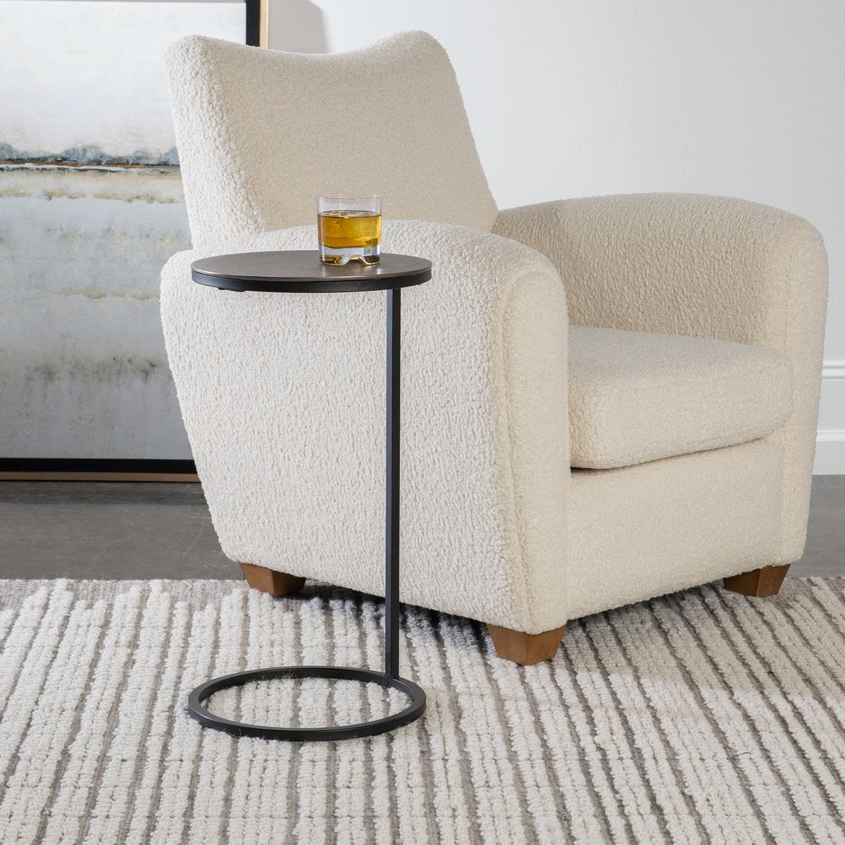 Beige armchair with a small round table and a glass of whiskey on a neutral background