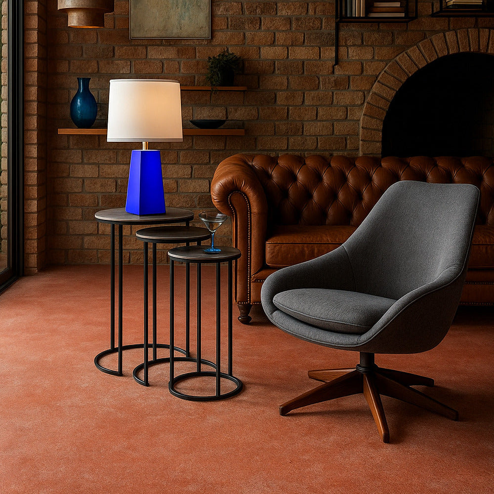 Modern interior with a gray chair, brown leather sofa, and a blue lamp against a brick wall.