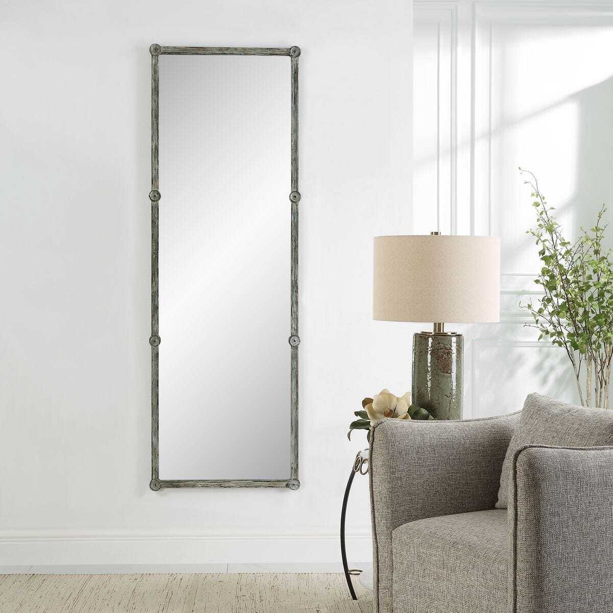 Decorative mirror on a white wall next to a gray sofa and lamp.