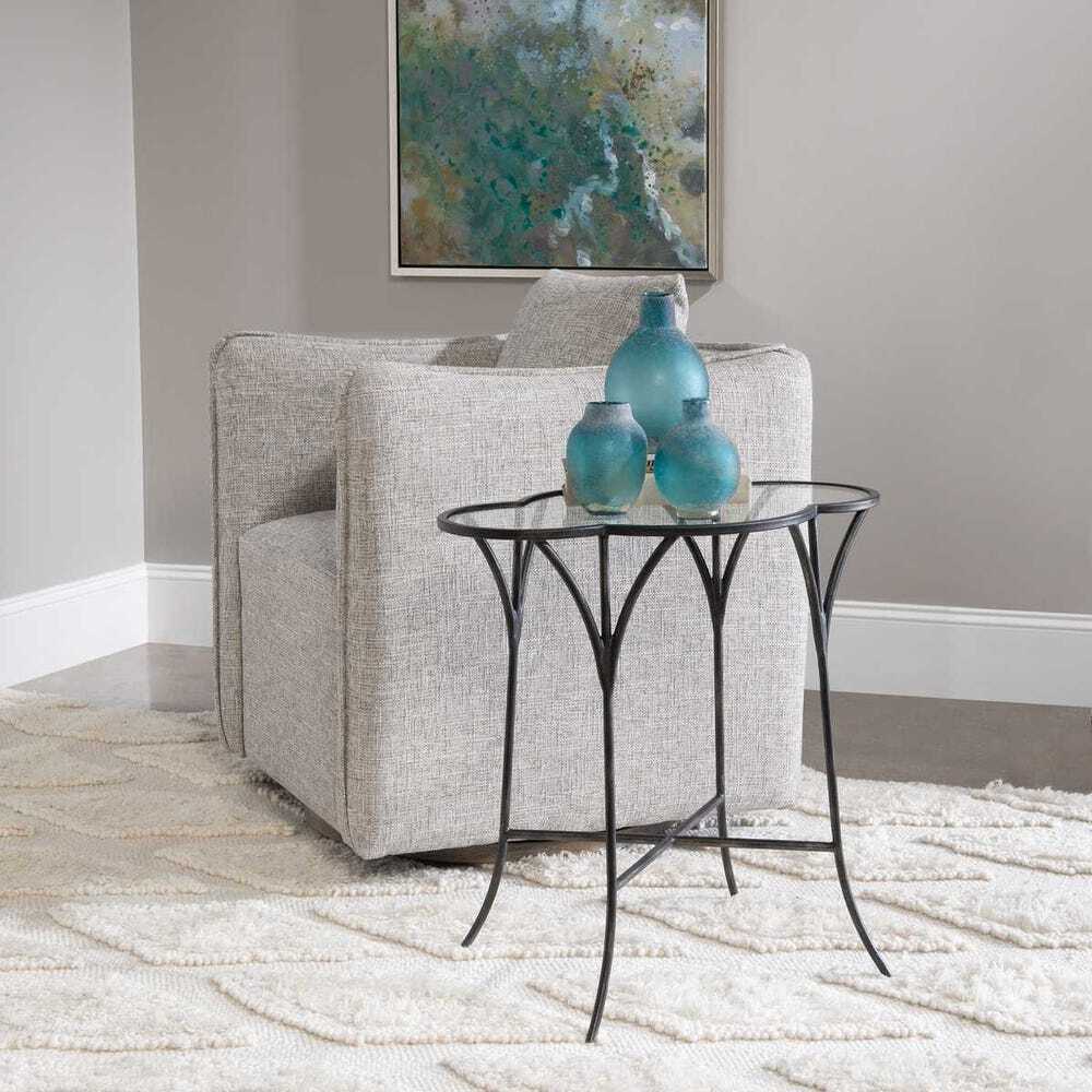 Gray armchair with a small black table and blue vases in a room with a painting on the wall.