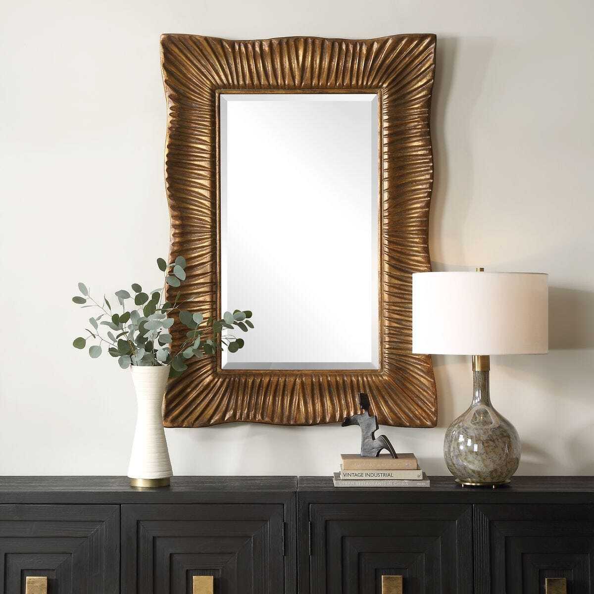 Decorative mirror with gold frame on a wall above a dark wooden console table.